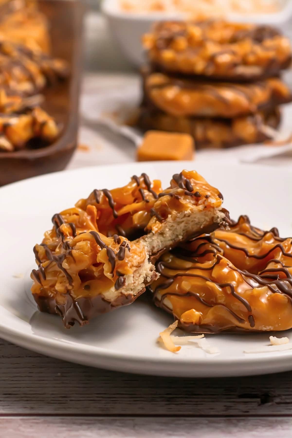 Two chocolate and caramel-drizzled cookies, one cut in half, on a white plate.