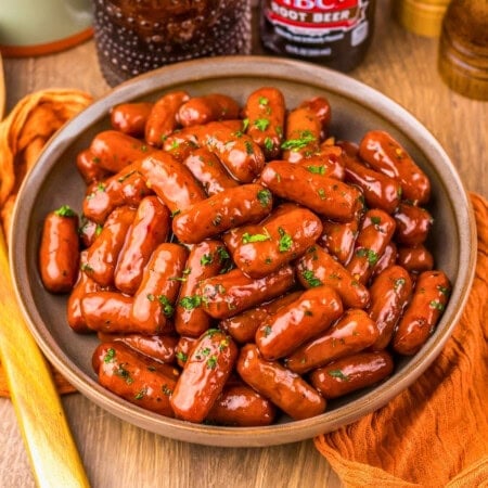 A bowl of cocktail sausages coated in sauce and garnished with chopped herbs.
