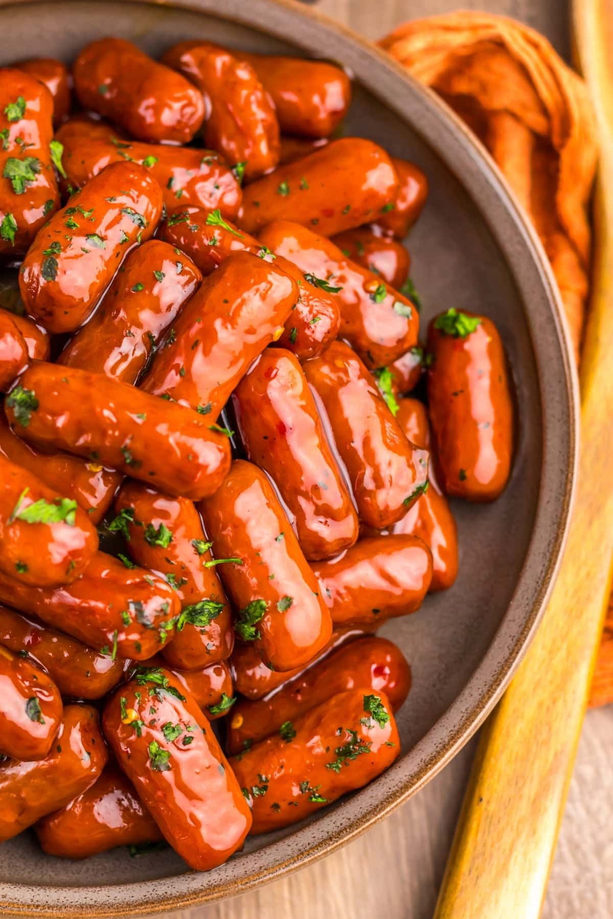 Cocktail sausages in a glossy sauce, garnished with chopped parsley in a bowl.