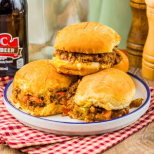 Three sloppy joe sandwiches on a plate with a bottle of root beer in the background.