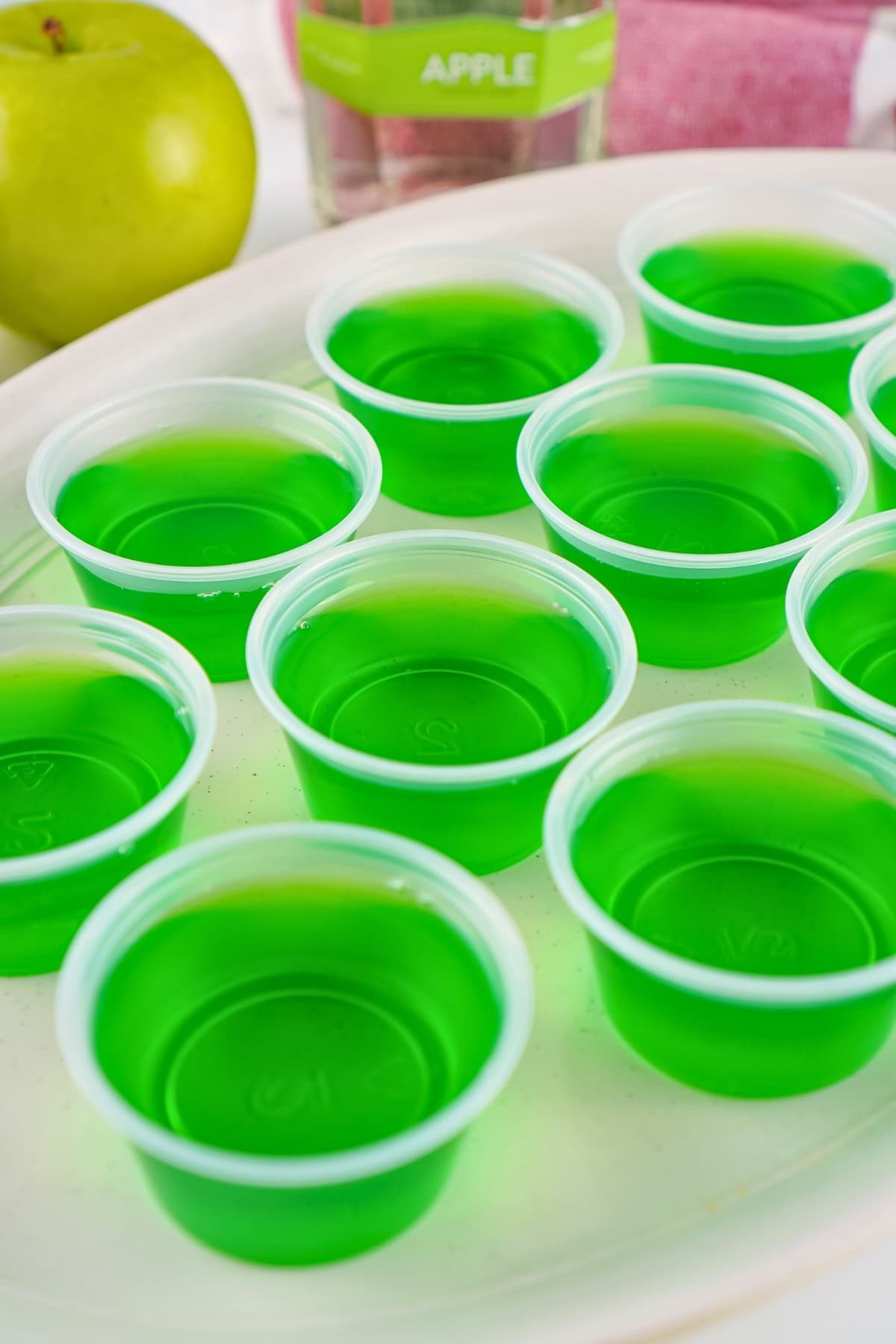 Small plastic cups filled with bright green gelatin on a white tray.