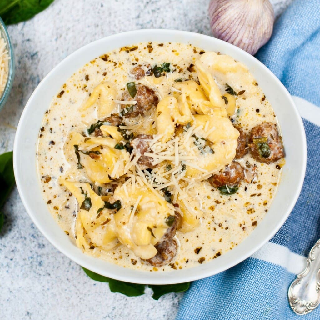 Creamy pasta soup with sausage, spinach, and shredded cheese in a white bowl.