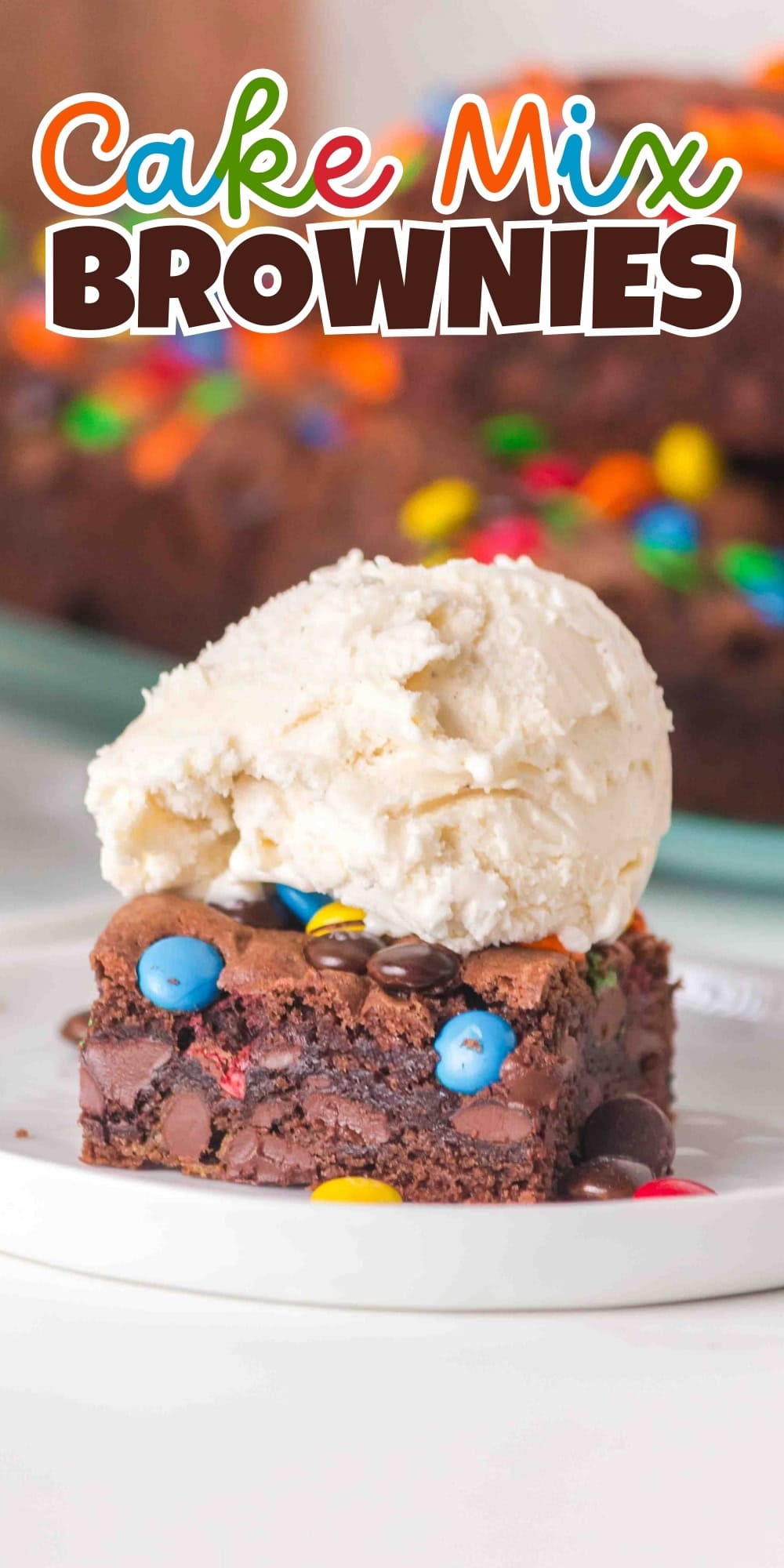 A brownie with candy pieces topped with vanilla ice cream on a white plate.