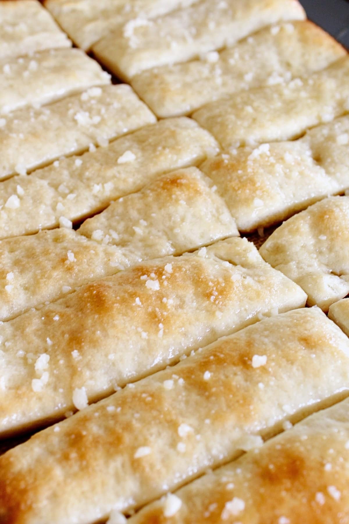 Golden baked breadsticks topped with coarse salt, arranged closely together.