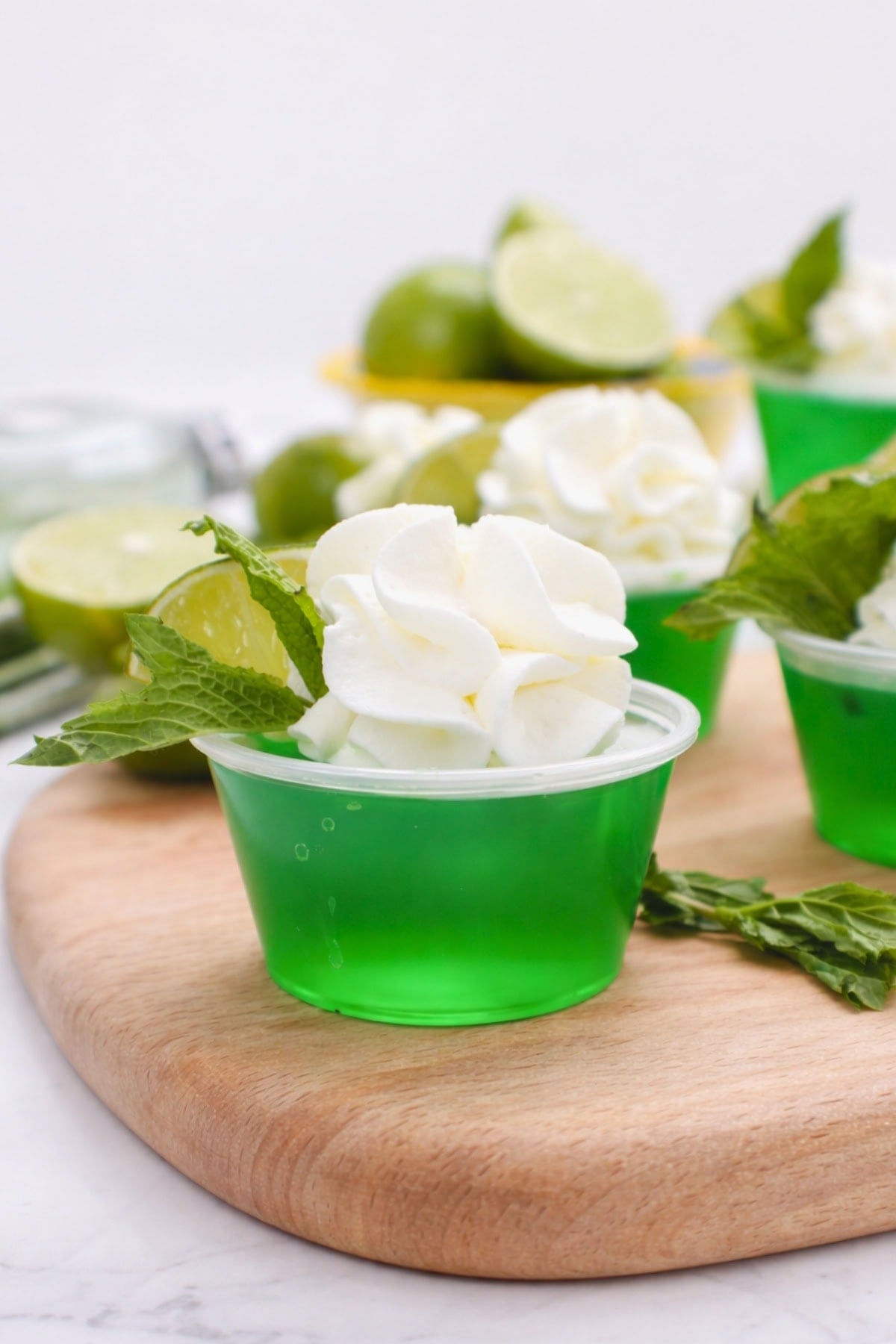 Green gelatin in a plastic cup, topped with whipped cream, lime, and mint leaves.