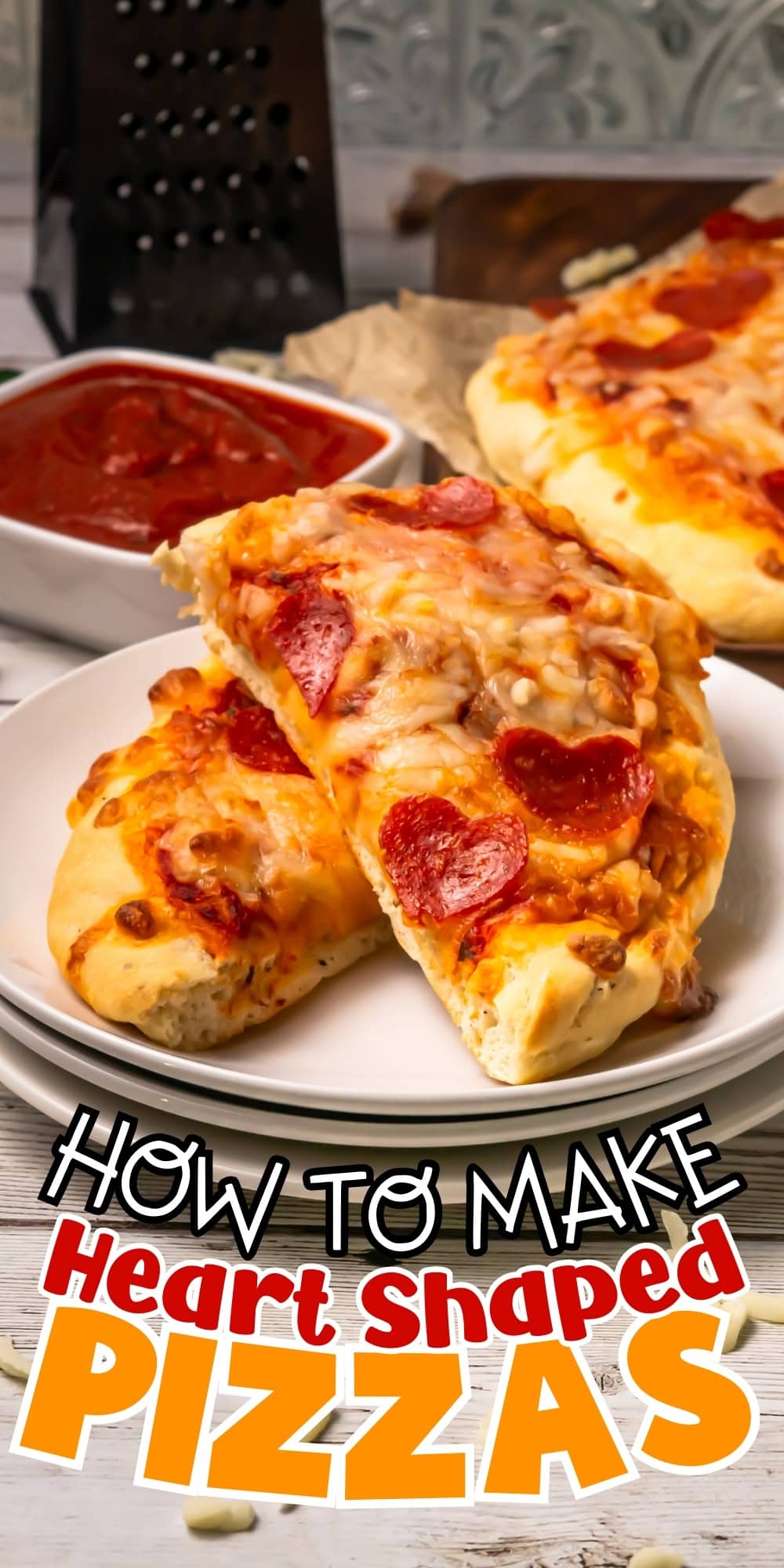 Two heart-shaped pepperoni pizzas on a plate with a bowl of marinara sauce.