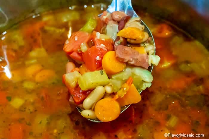 A ladle of vegetable and bean soup with visible carrots, celery, and beans.