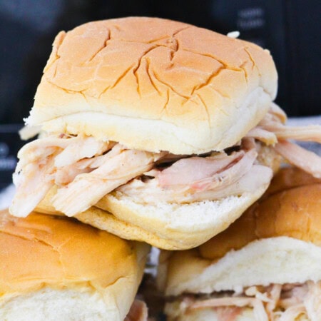 Three shredded chicken sandwiches on soft hamburger buns, stacked together.