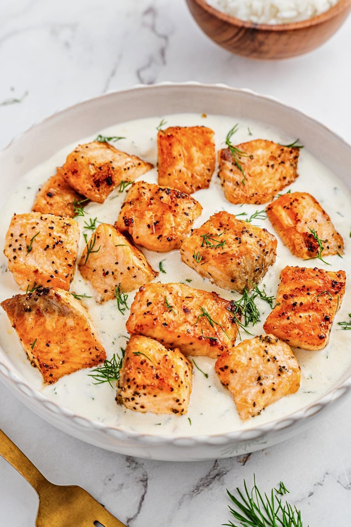 Seared salmon pieces in a creamy white sauce, garnished with fresh dill.