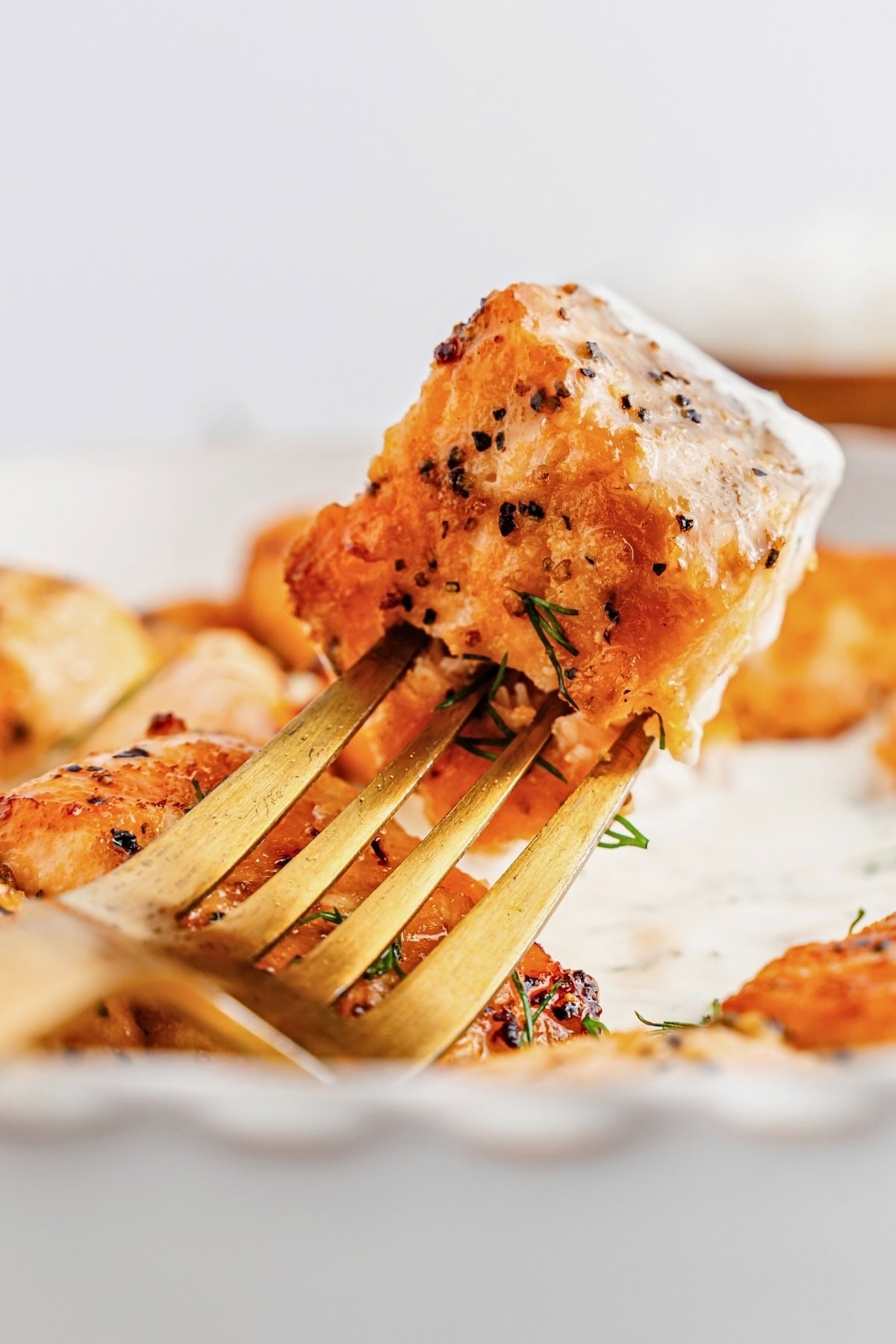 A golden fork holding a piece of seasoned, saucy chicken against a white background.