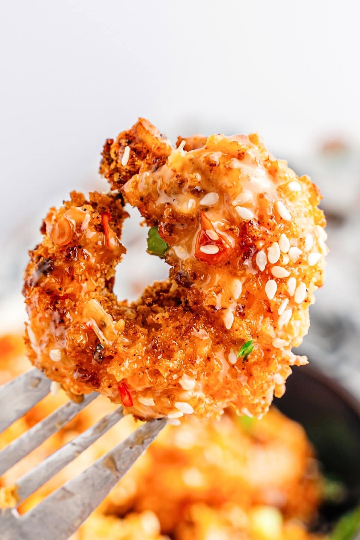 A close-up of a breaded, sesame-coated shrimp on a fork.