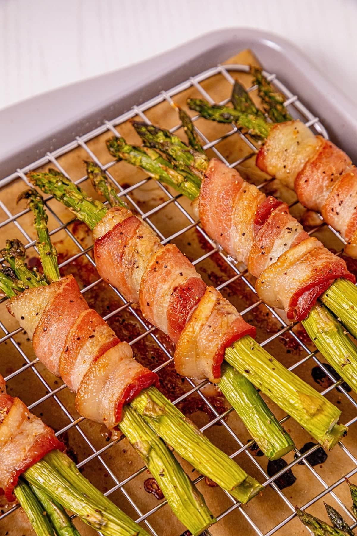 Bacon-wrapped asparagus bundles on a wire rack over a baking sheet.