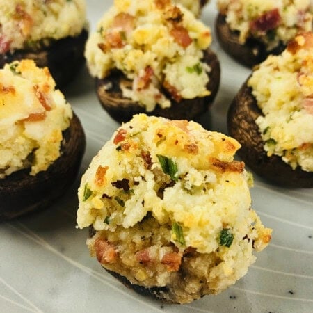 Stuffed mushrooms with a golden cheesy breadcrumb and herb topping on a plate.