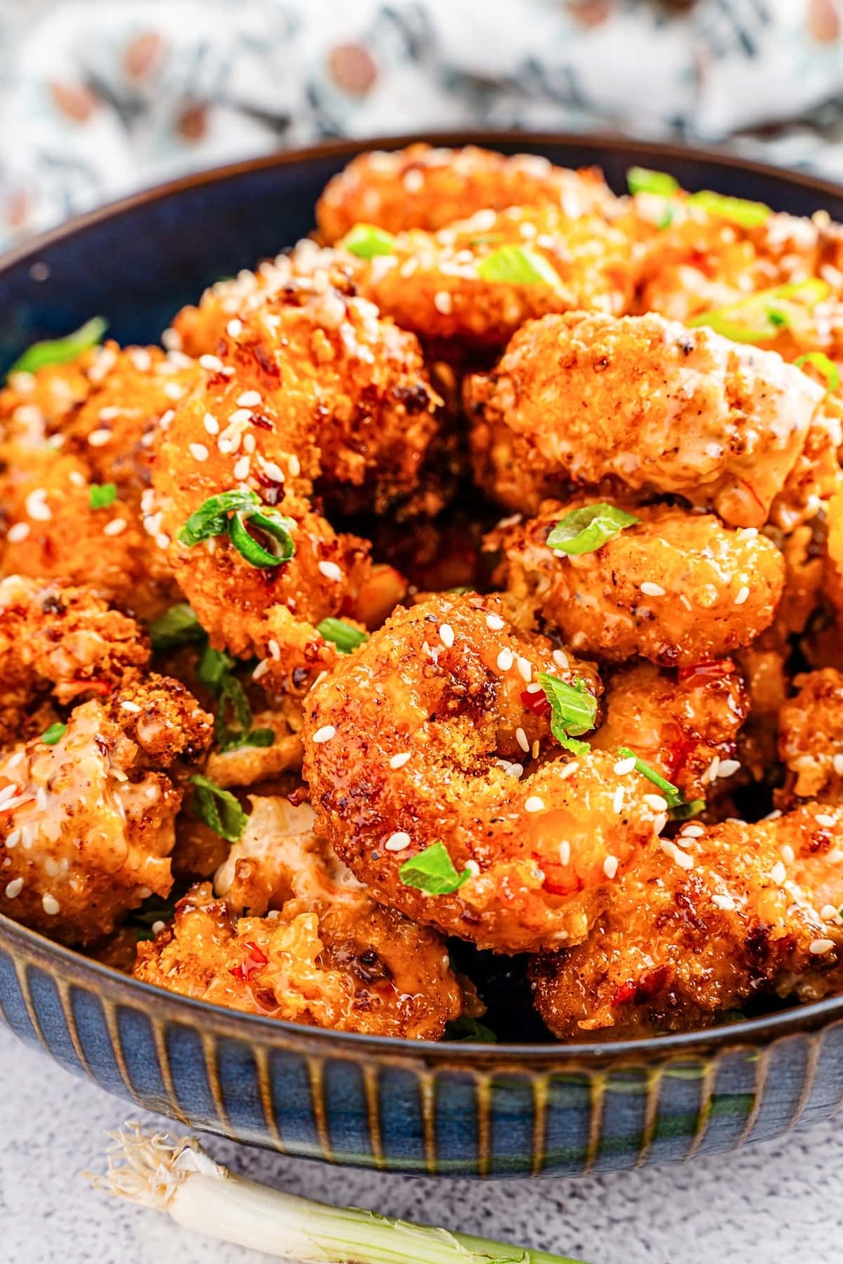 A bowl of crispy fried shrimp topped with sesame seeds and chopped green onions.