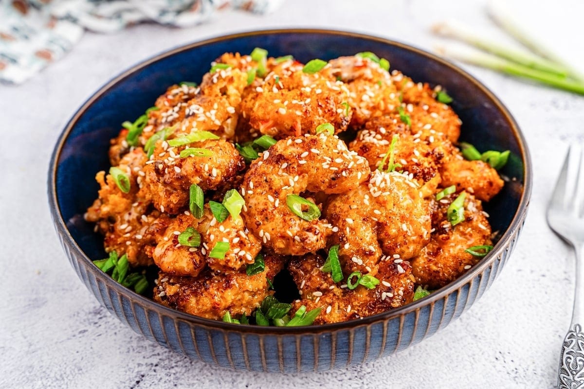 A bowl of crispy fried shrimp garnished with sesame seeds and chopped green onions.