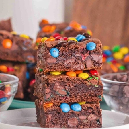 Three chocolate brownies with colorful candies stacked on a white plate.
