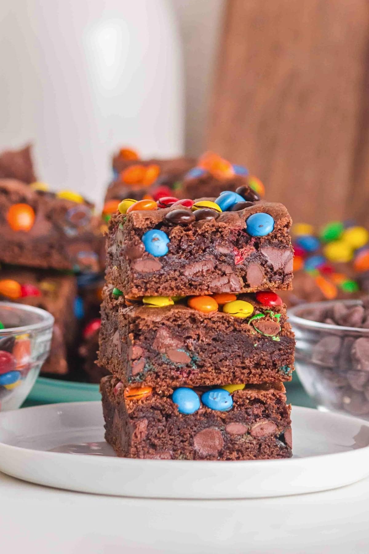 Three chocolate brownies with colorful candies stacked on a white plate.
