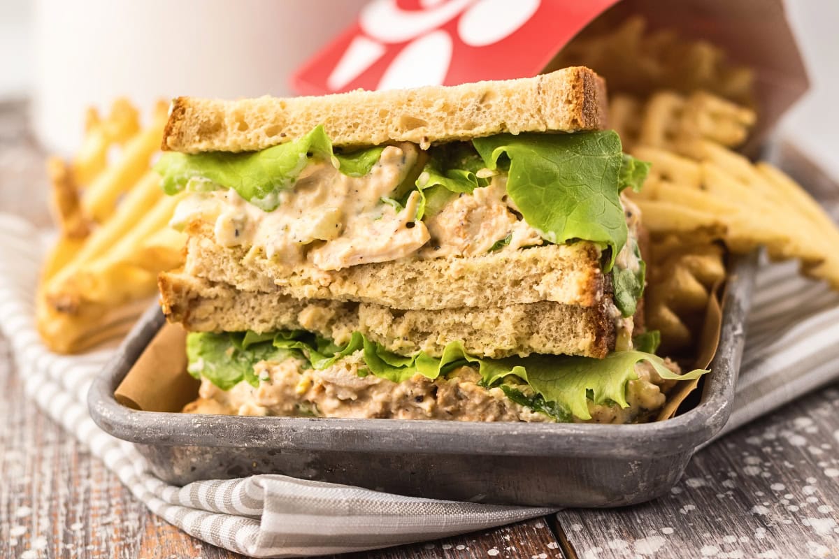 Chicken salad sandwich with lettuce, served with waffle fries in a metal tray.