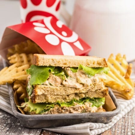 Chicken salad sandwich with lettuce and waffle fries in a tray on a striped napkin.