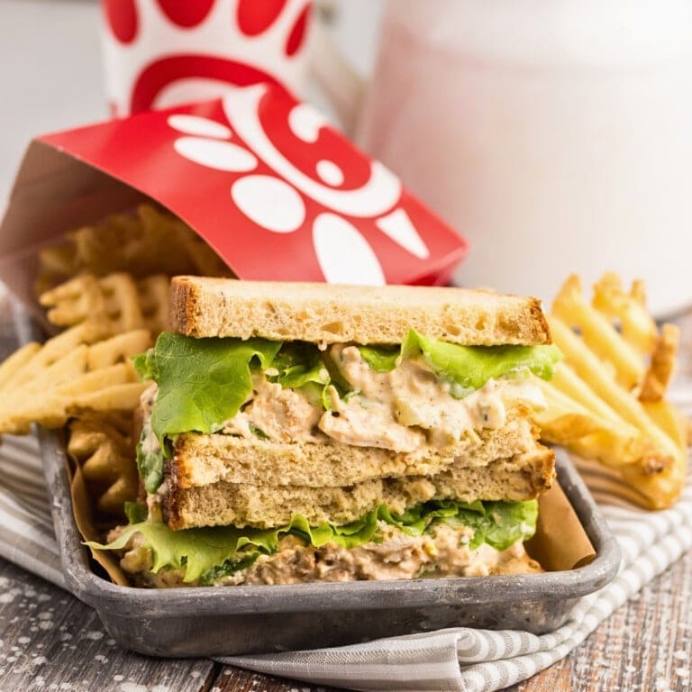 Chicken salad sandwich with lettuce and waffle fries in a tray on a striped napkin.