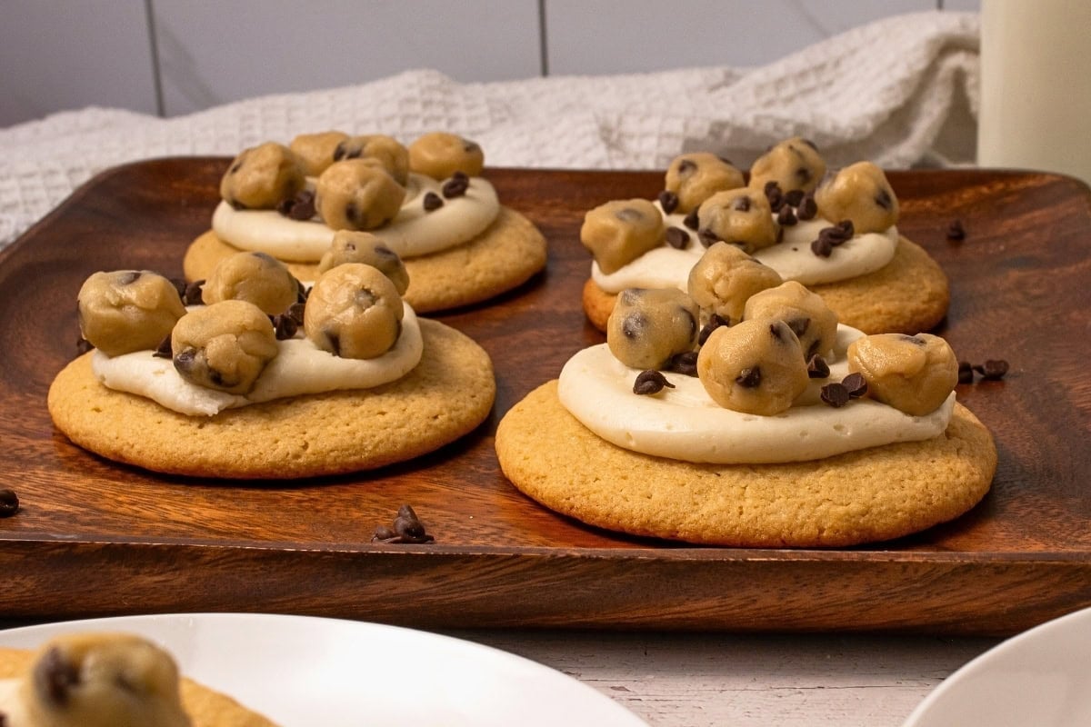 Cookies topped with frosting and small chocolate chip cookie dough balls on a tray.