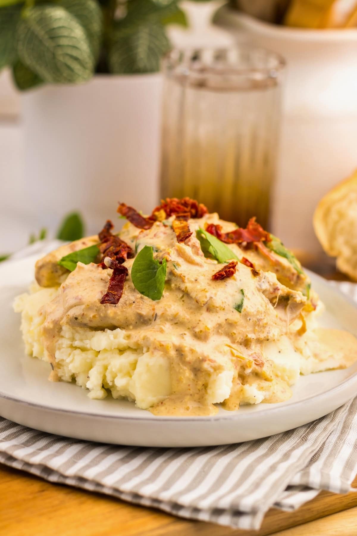 Mashed potatoes with Tuscan chicken topped with creamy sauce, herbs, and sun-dried tomatoes on a plate.
