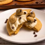 A cookie topped with frosting, cookie dough balls, and chocolate chips on a plate.
