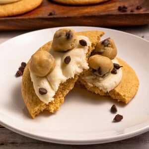 A cookie topped with frosting, cookie dough balls, and chocolate chips on a plate.