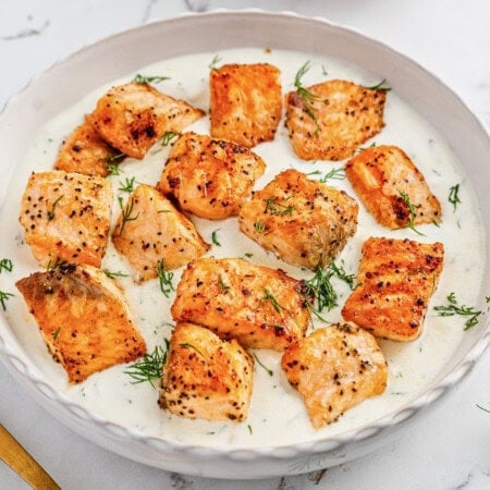 Seared salmon pieces in creamy white sauce, garnished with fresh dill.