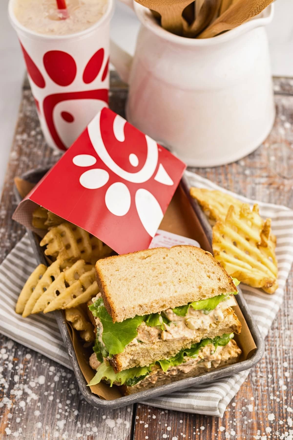 Chick-fil-A sandwich with waffle fries and a drink on a rustic wooden surface.
