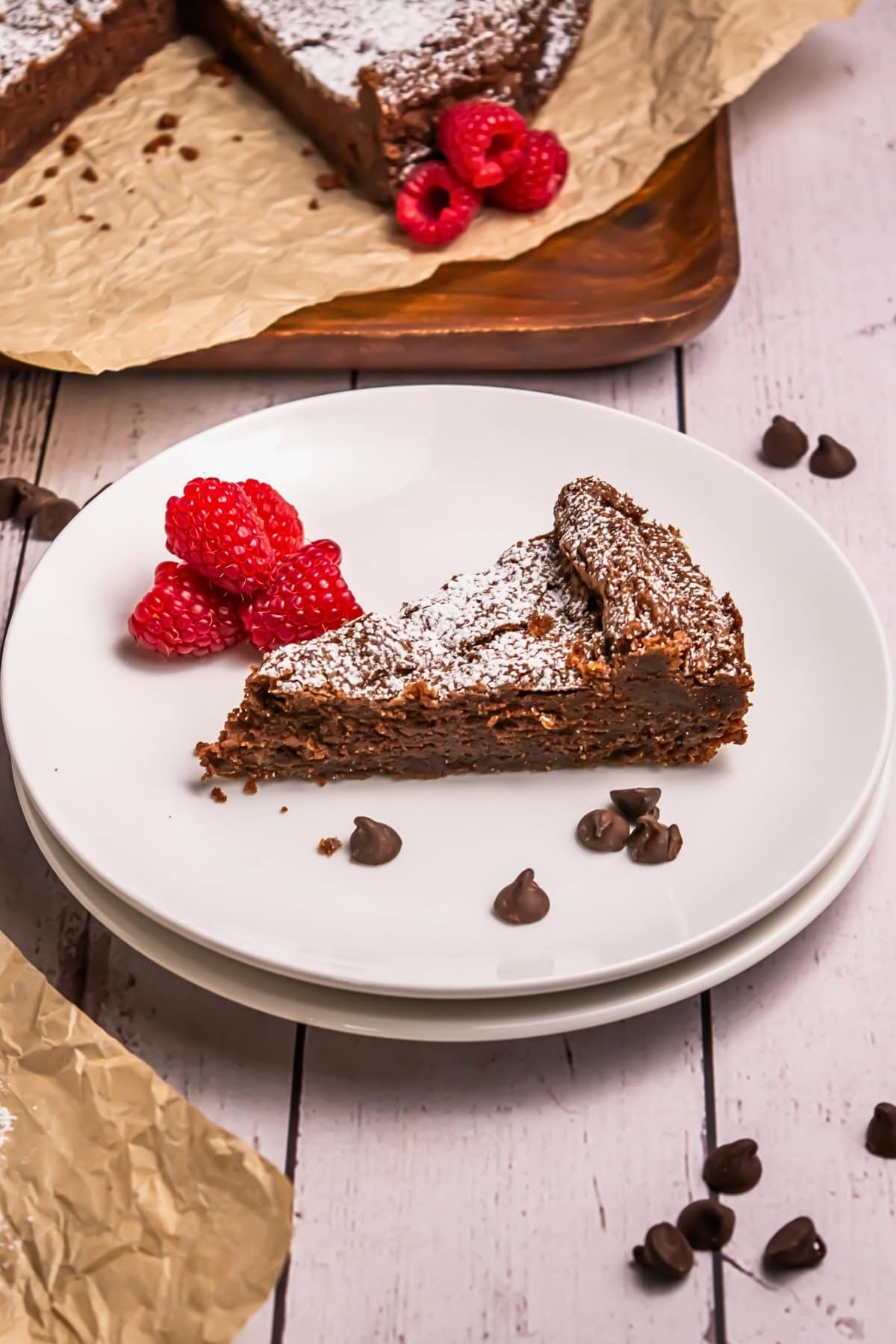 A slice of chocolate cake with raspberries and chocolate chips on a white plate.