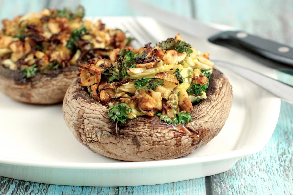 Stuffed mushrooms with herbs and nuts on a white plate with a knife and fork.