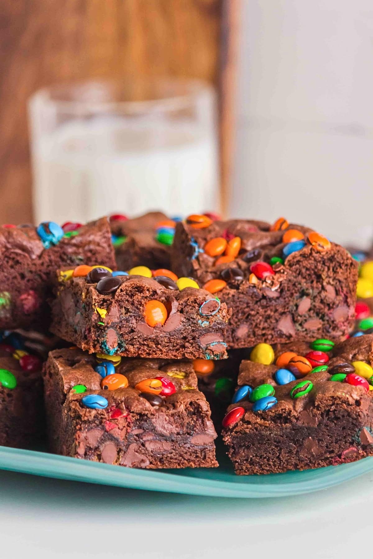 Brownies topped with colorful candy-coated chocolates on a plate, with milk behind.