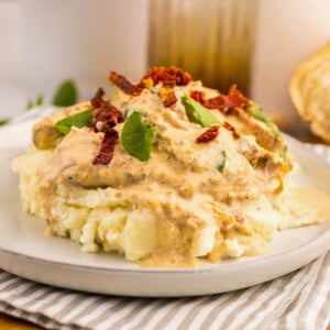 Mashed potatoes with Tuscan chicken topped with creamy sauce, herbs, and sun-dried tomatoes.