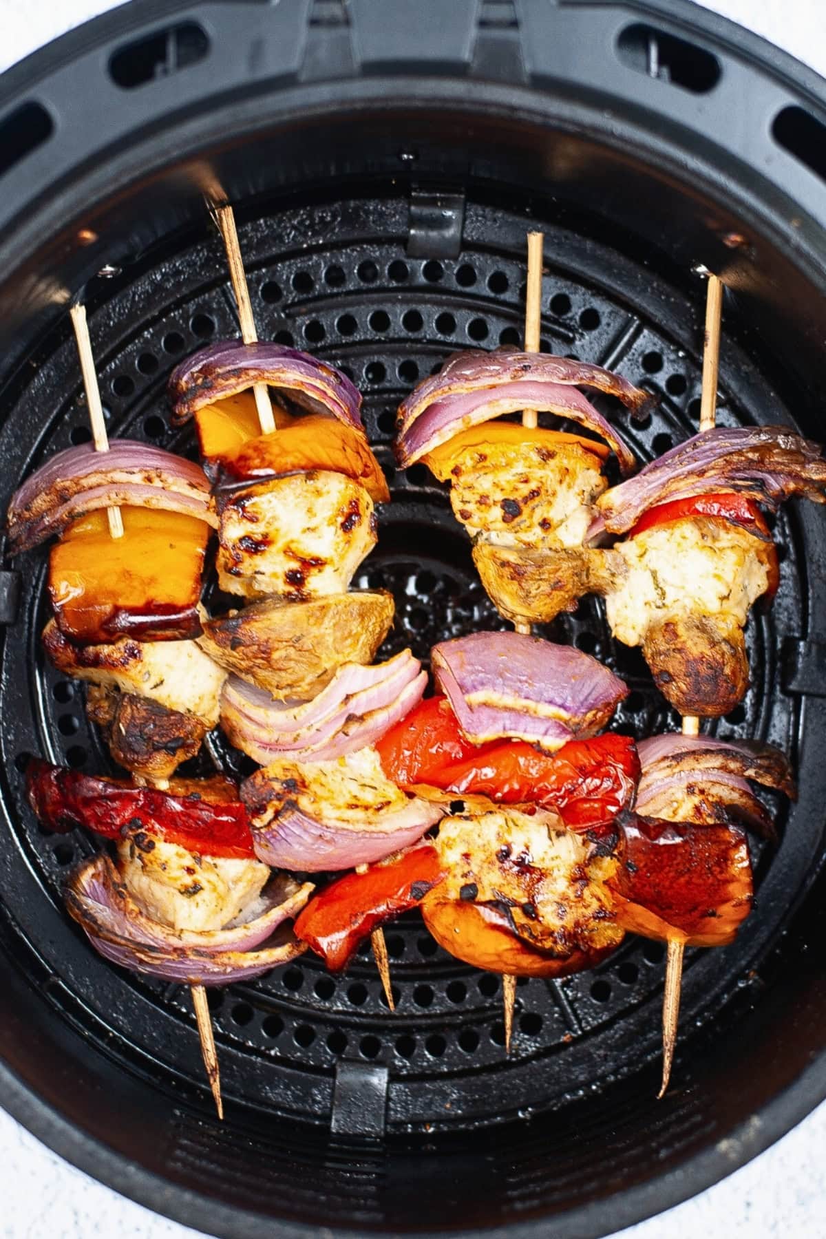 Chicken and vegetable skewers grilled in an air fryer basket.