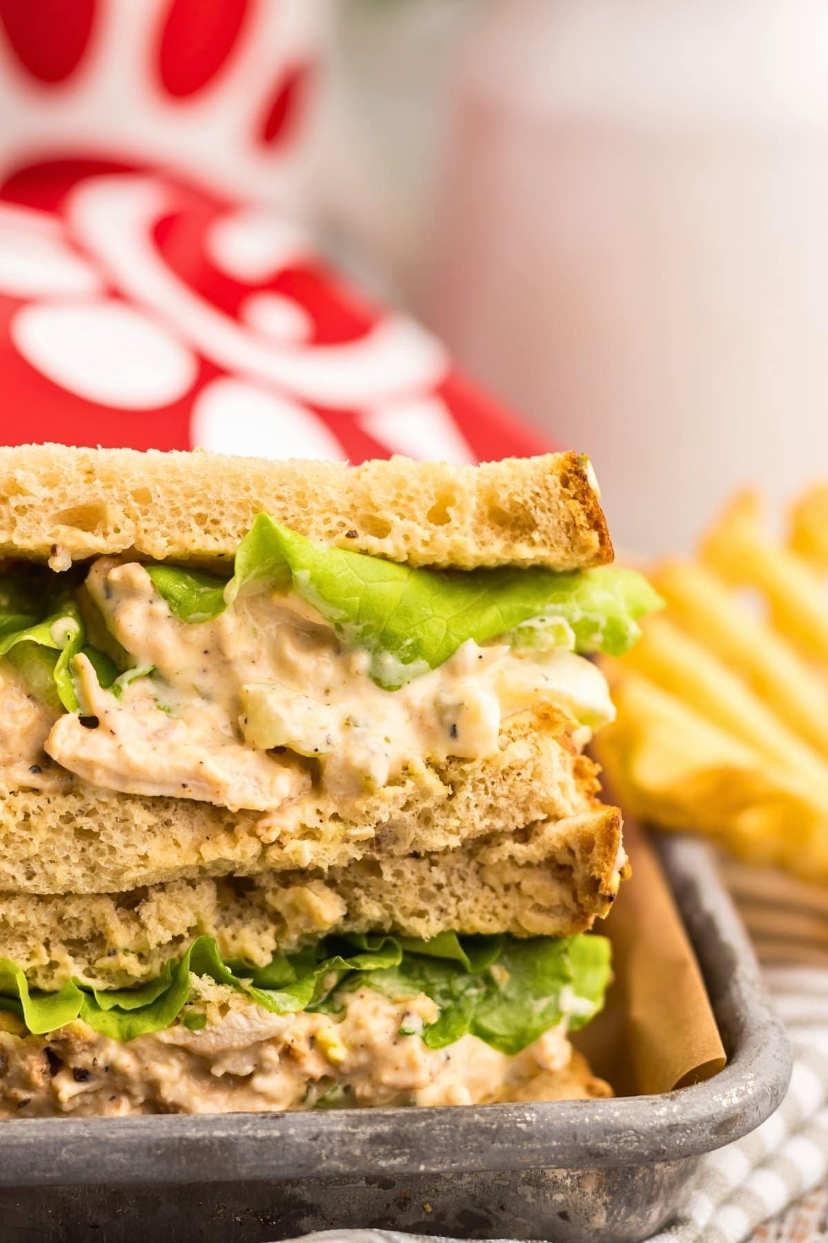 A stacked chicken salad sandwich with lettuce on toasted bread, next to chips.