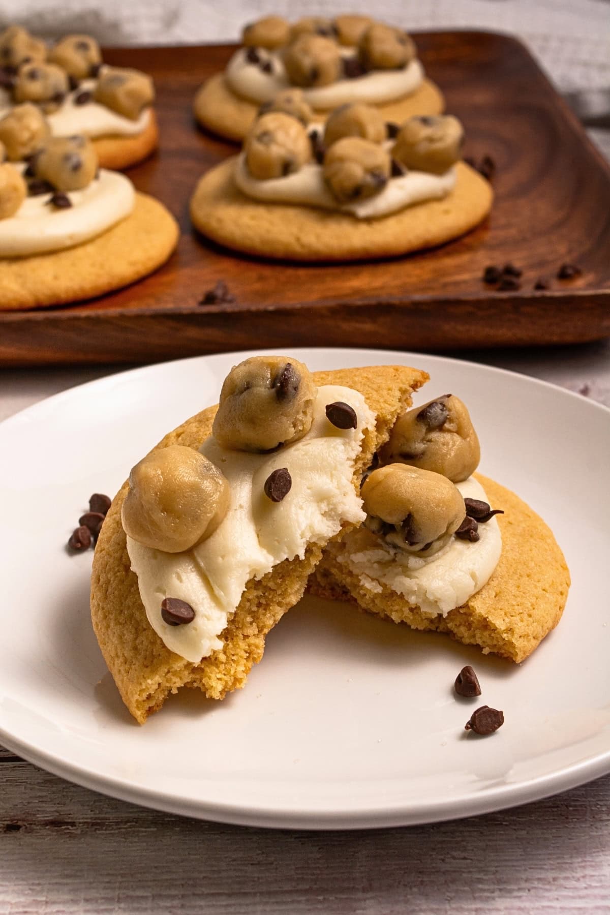 A cookie with frosting and cookie dough balls, broken in half on a white plate.