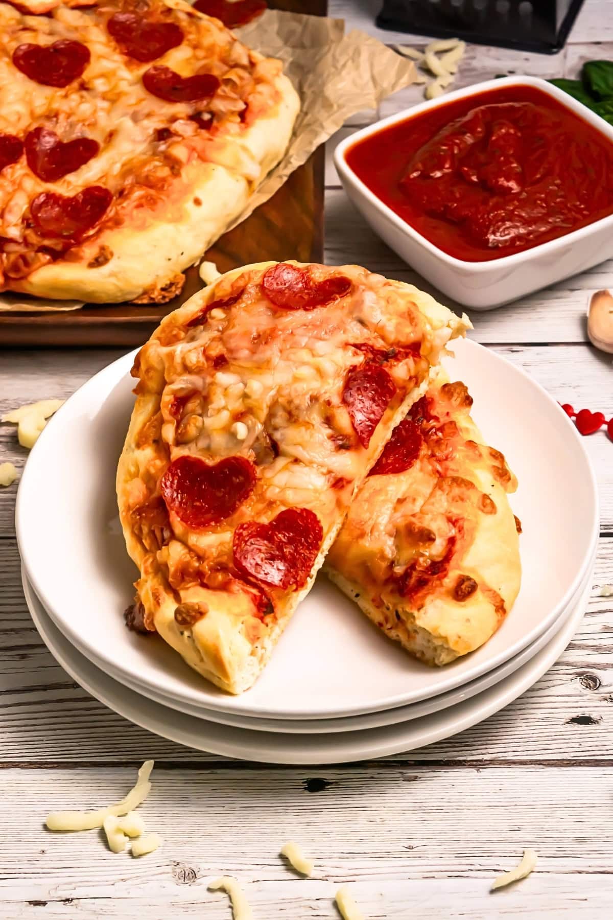 Two heart-shaped pepperoni pizzas on stacked white plates with marinara sauce.