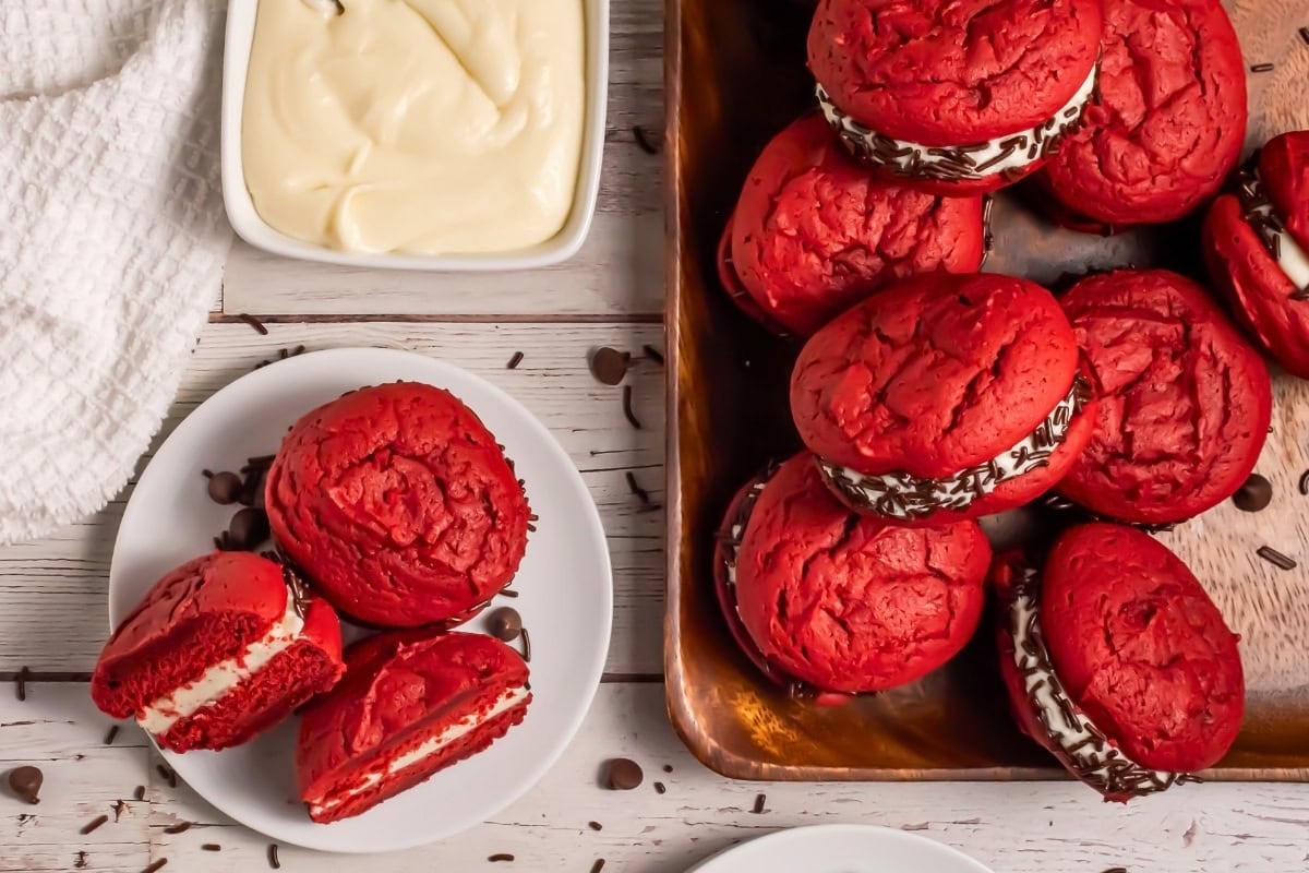 Red velvet whoopie pies with cream filling and chocolate chips on a table.
