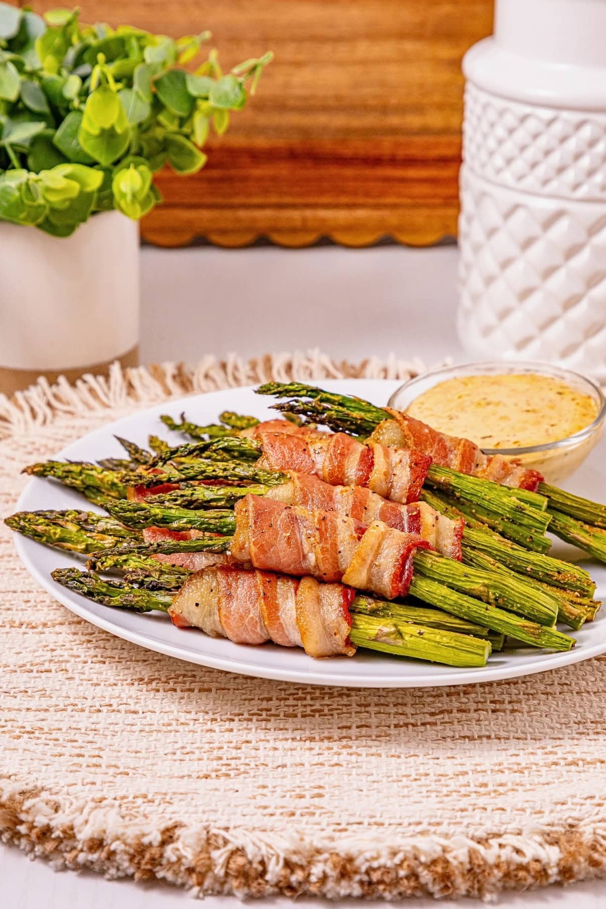 Bacon-wrapped asparagus on a white plate with dipping sauce.