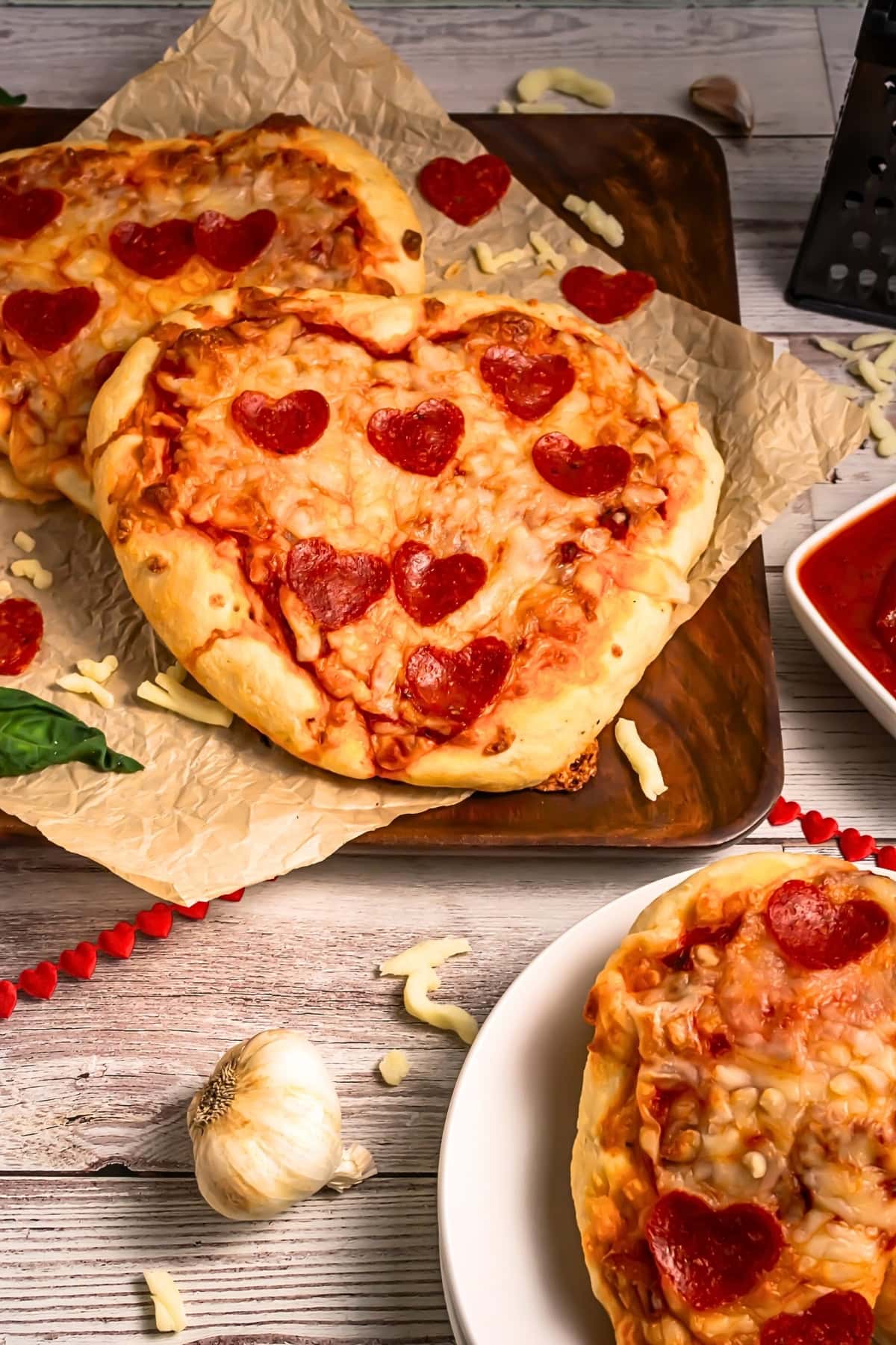 Heart-shaped pepperoni pizzas on parchment paper and white plates.