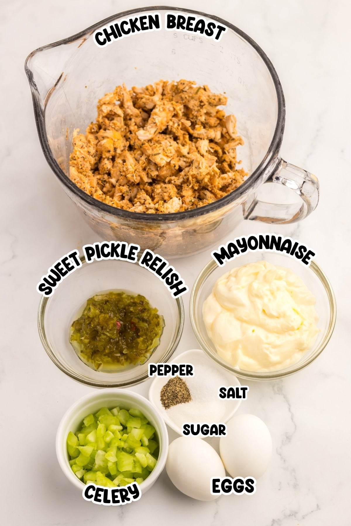 Bowls of chicken breast, mayo, relish, celery, eggs, and seasonings on a counter.
