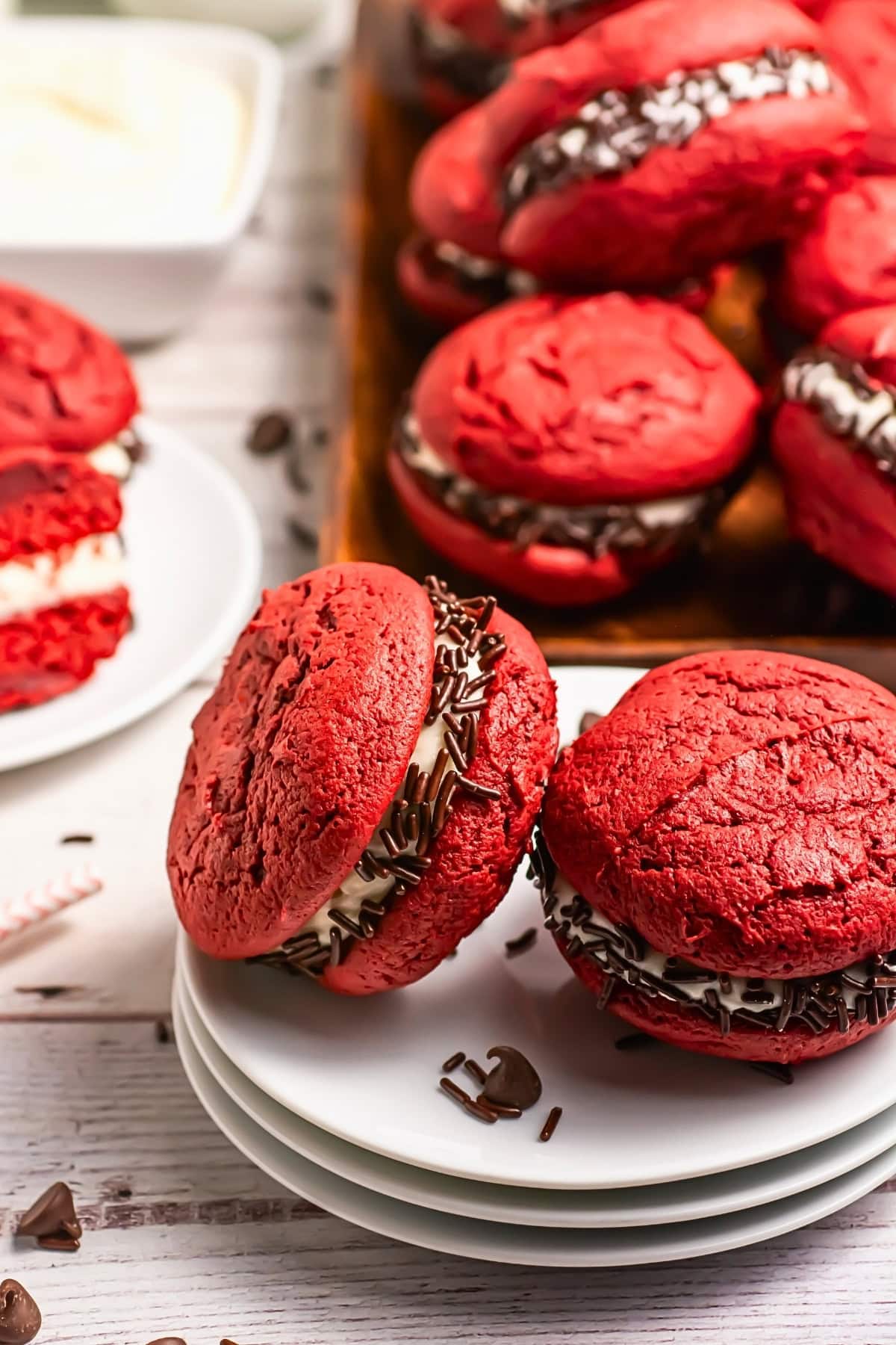 Red velvet whoopie pies with cream filling and chocolate sprinkles on plates.