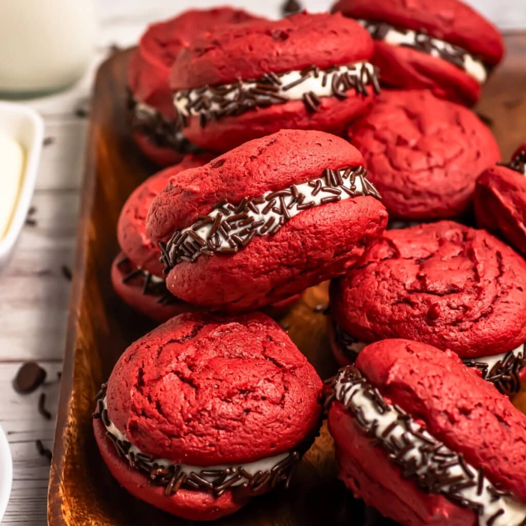 Red velvet whoopie pies with cream filling and chocolate sprinkles on a wooden tray.