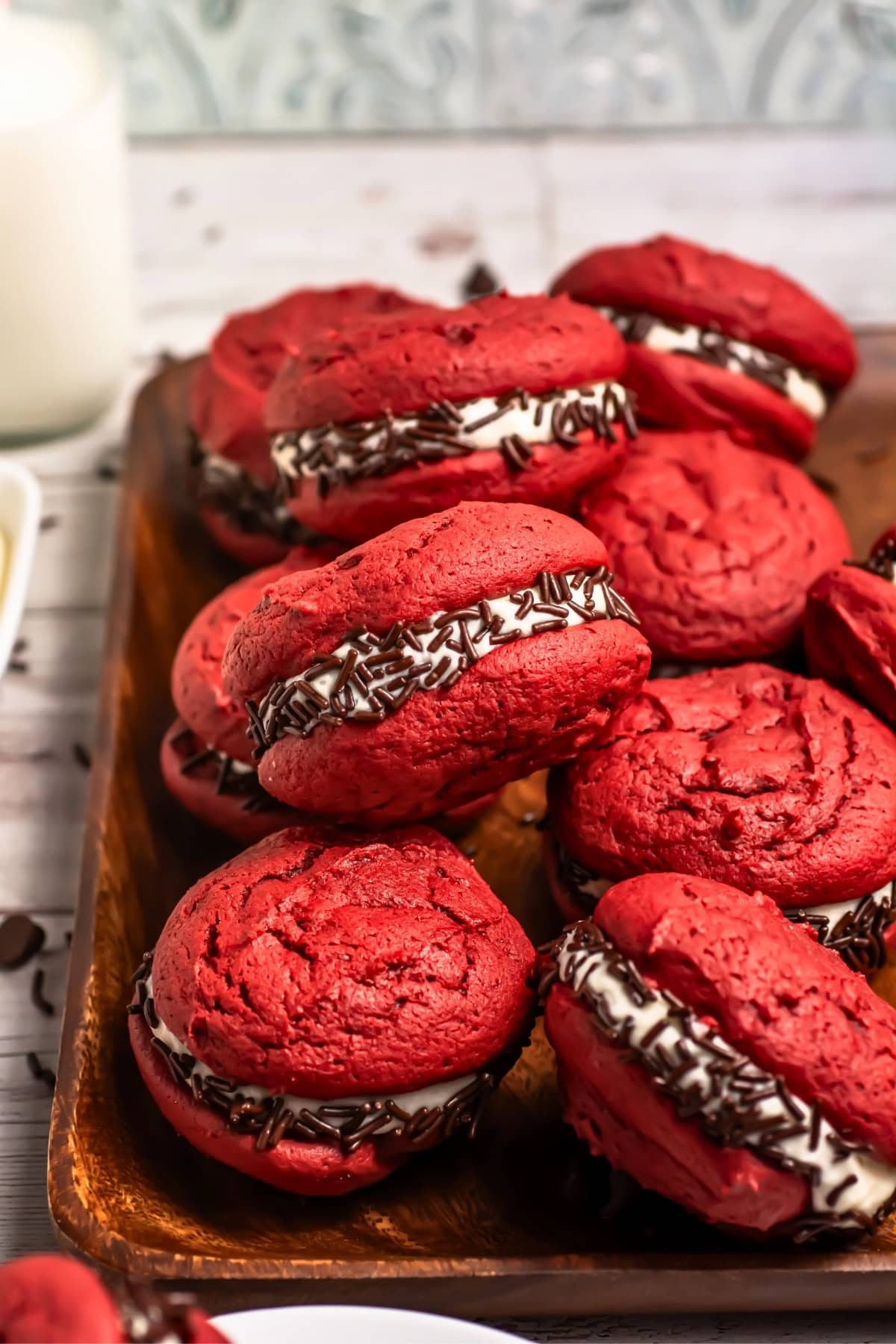 Red sandwich cookies with cream filling and chocolate sprinkles on a wooden tray.