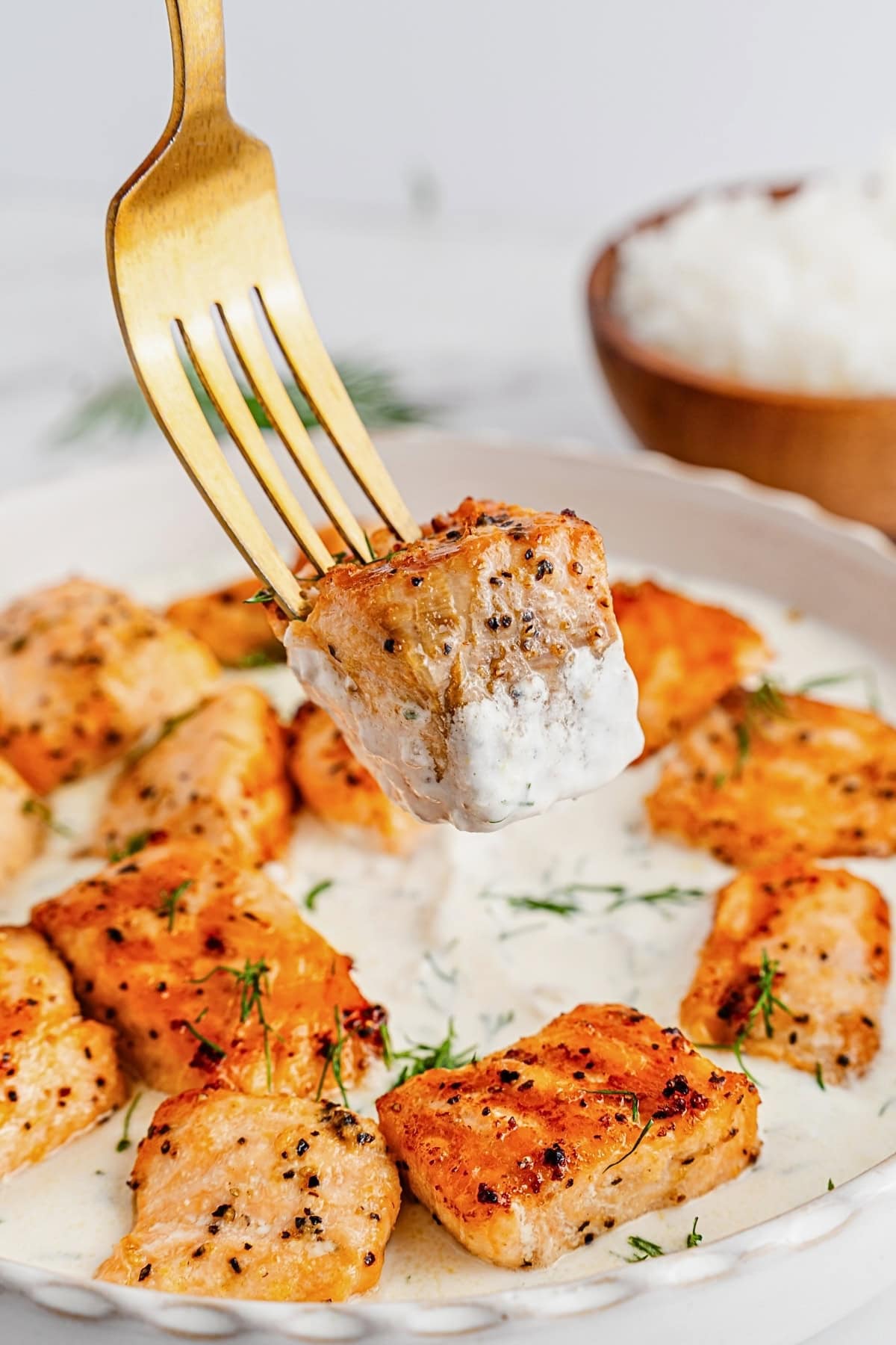 Golden salmon bites on a creamy sauce, one piece on a fork, rice in background.