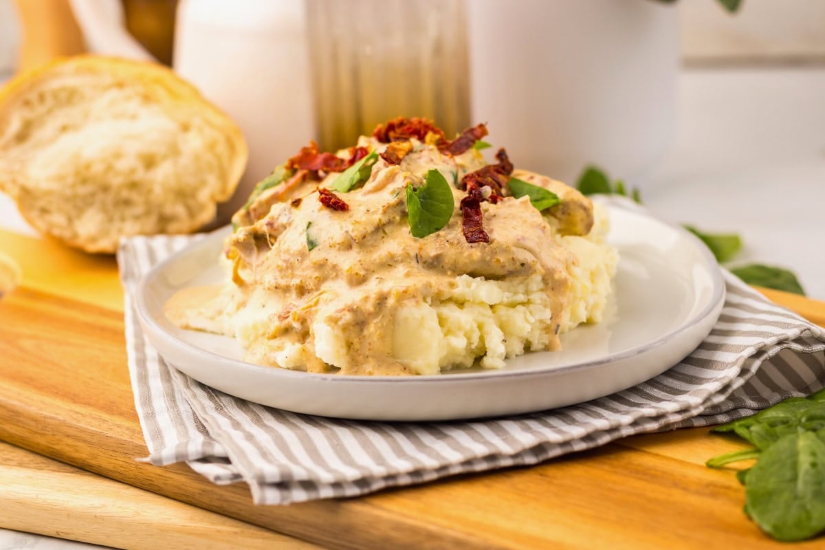 Tuscan chicken topped with creamy sauce, herbs, and sun-dried tomatoes on a plate.