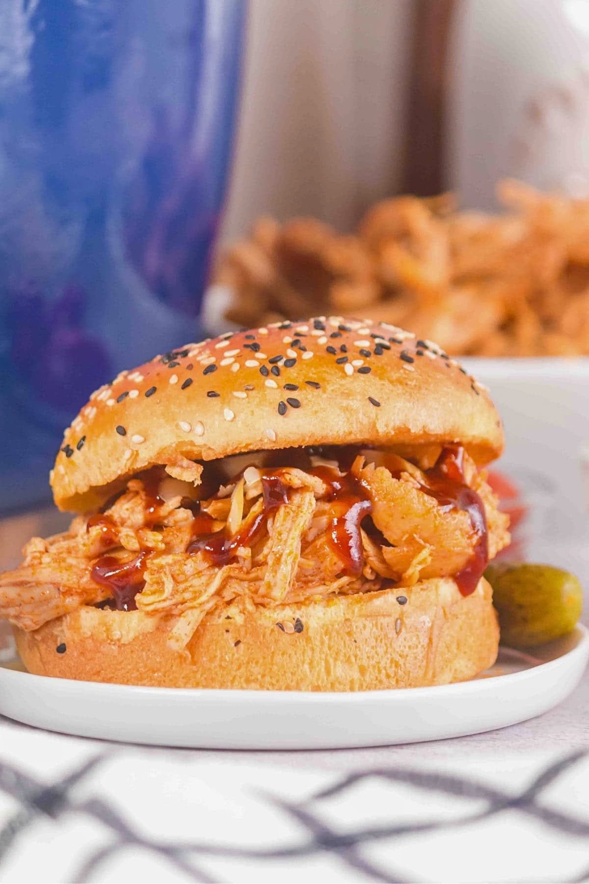 Pulled chicken sandwich with barbecue sauce on a sesame bun, served on a plate.