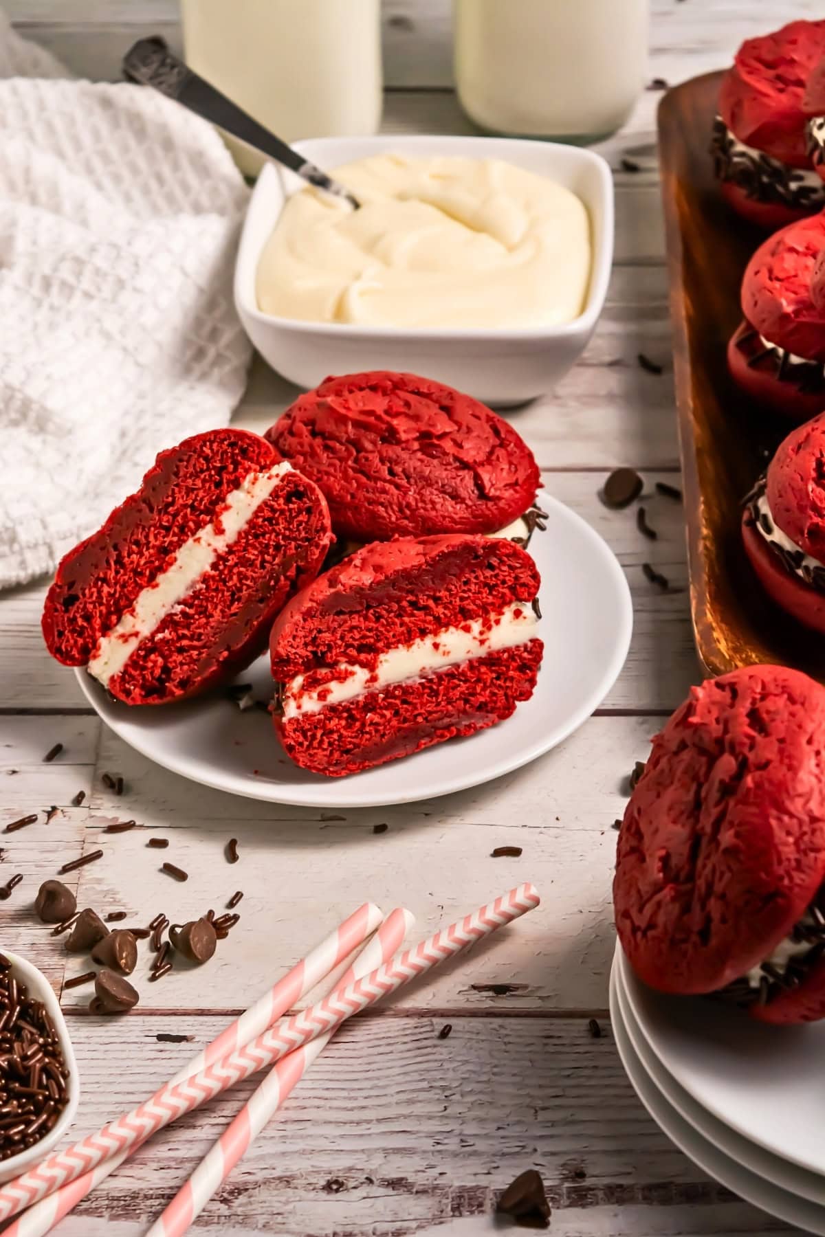 Red velvet whoopie pies with cream filling on a plate, surrounded by ingredients.