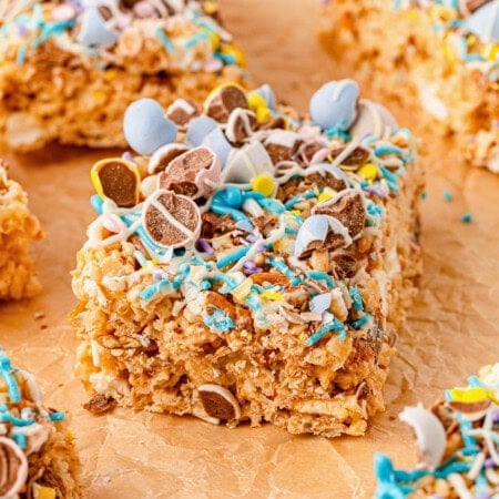 A rice crispy treat topped with colorful candy and chocolate pieces on parchment paper.